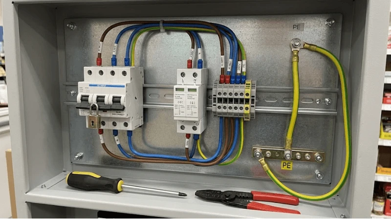 Close-up of kiosk AC power-entry components mounted on a DIN rail or metal backplate with realistic wiring, ferrules, earth bond and service disconnect